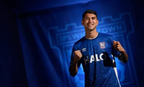 Игрок в форме Ipswich Town на фоне логотипа клуба