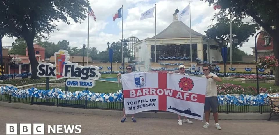 Два человека с флагом Barrow AFC у входа в Six Flags