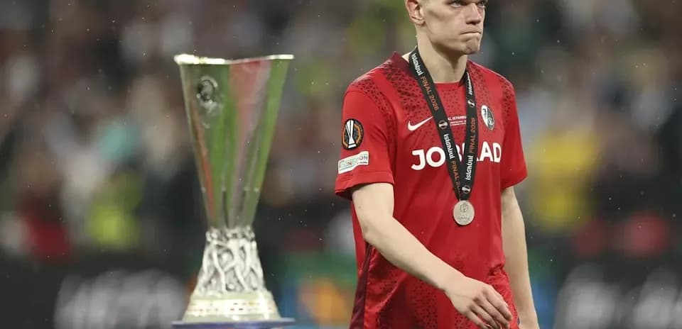 Игрок с медалью проходит мимо трофея Лиги Европы